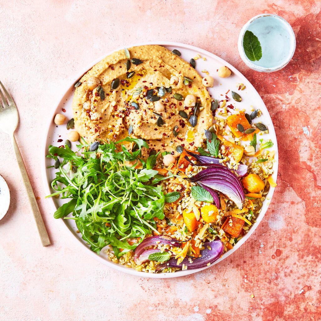 Vibrant harissa hummus bowl topped with fresh vegetables, roasted chickpeas, and herbs, a healthy Mediterranean food trend for 2026.