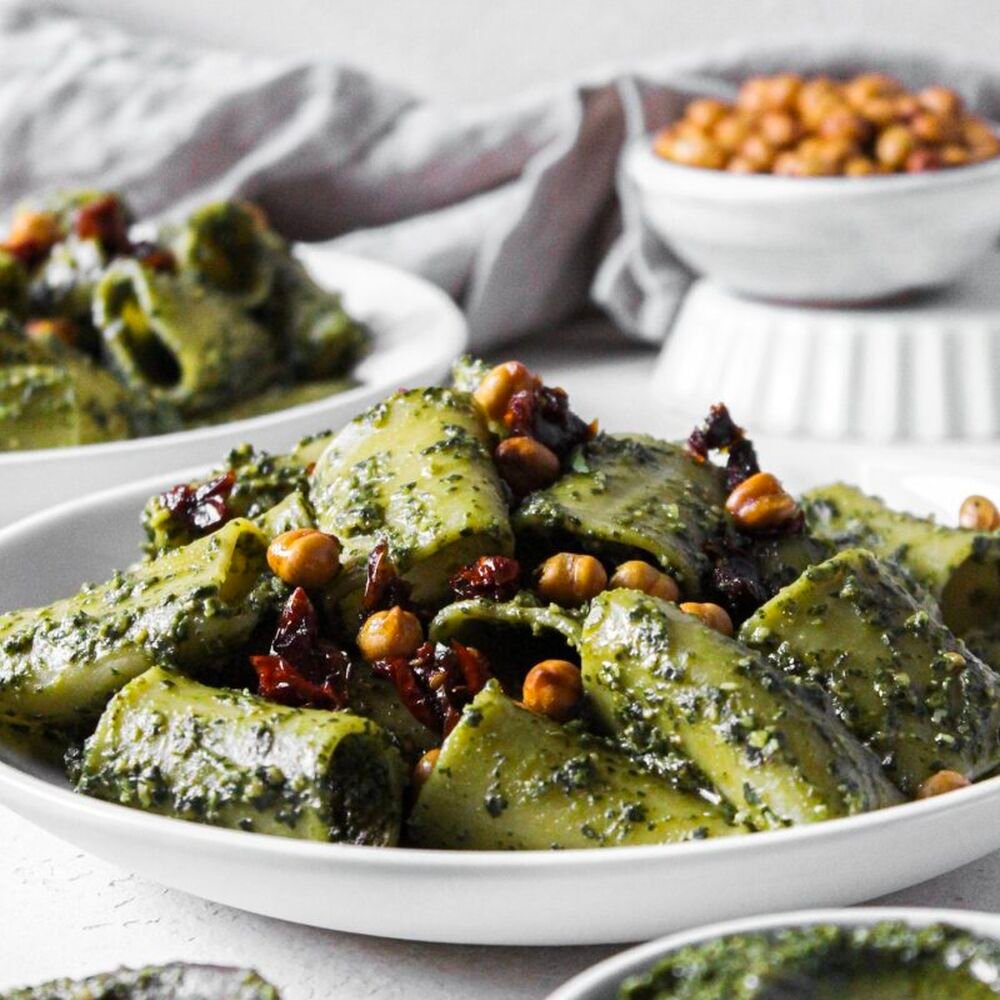 Green dandelion pesto pasta bowl topped with herbs and roasted chickpeas, representing a sustainable US food trend for 2026.